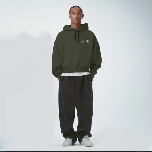 Person wearing a Olive green hoodie and black pants on a white background