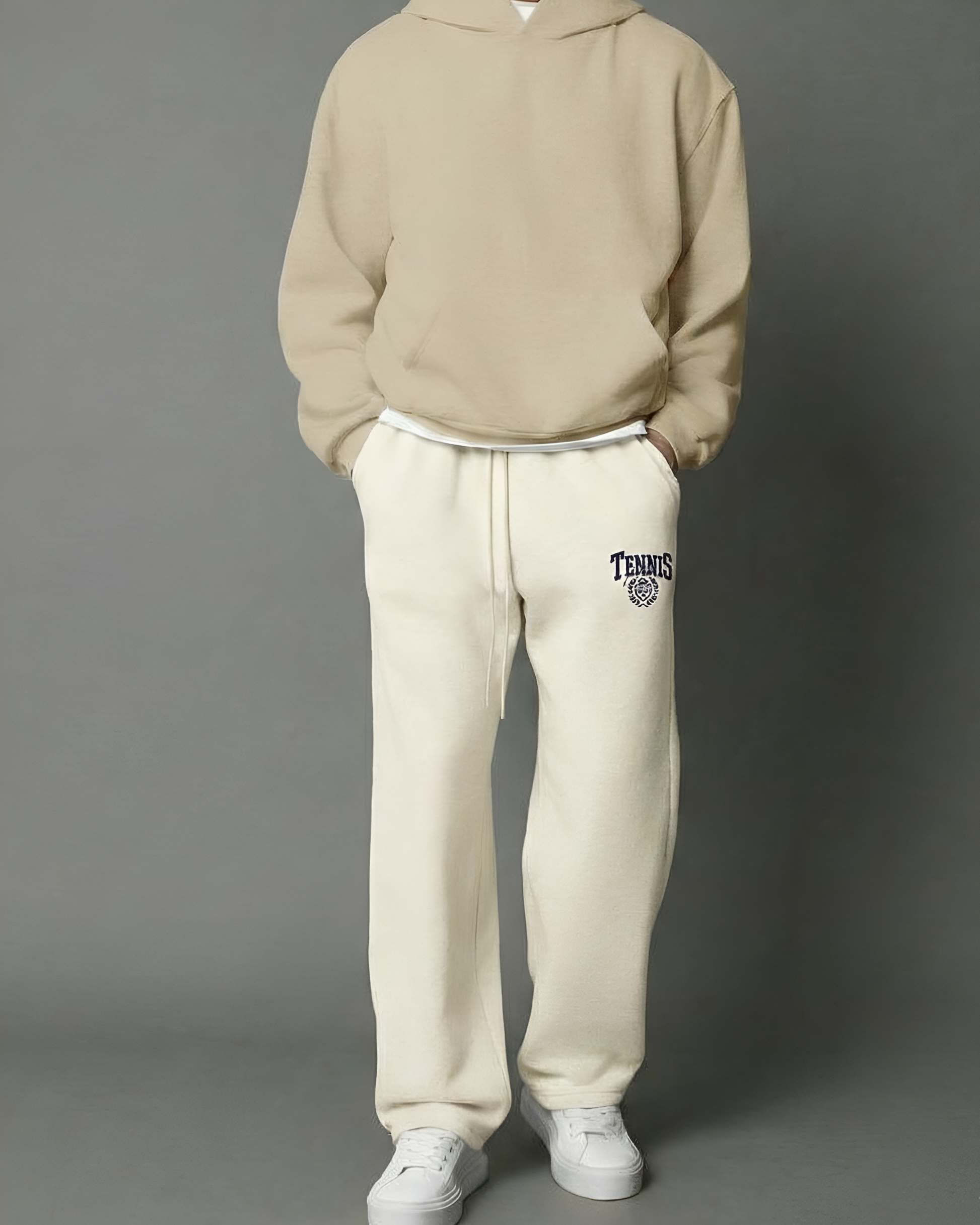 Person wearing a beige hoodie and white sweatpants with a logo on a gray background